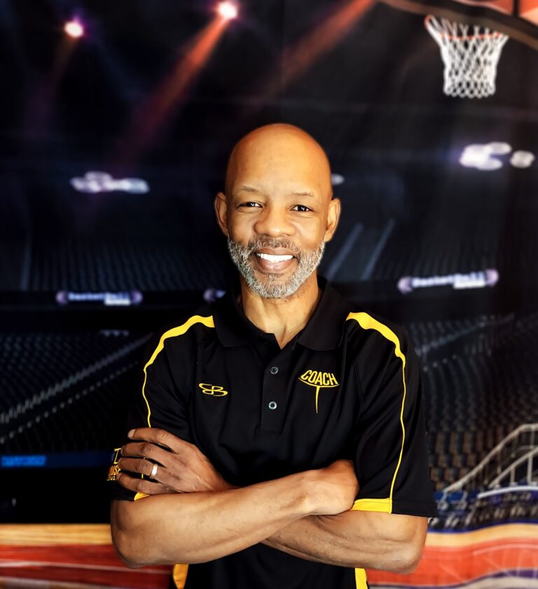 Coach T with arms crossed in front of an arena backdrop