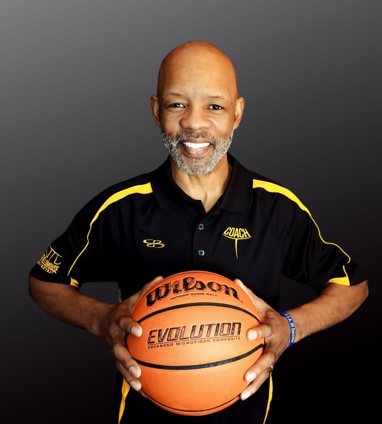 Coach T holding a basketball in a black and gold coaching polo