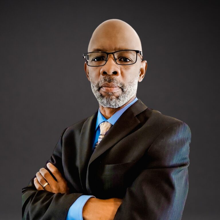 Antwaun Coach T Thompson in a dark suit and glasses, arms crossed